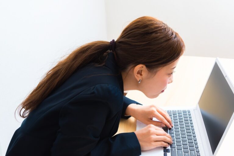 デスクで首を突き出した前かがみの姿勢でパソコンを打つ女性