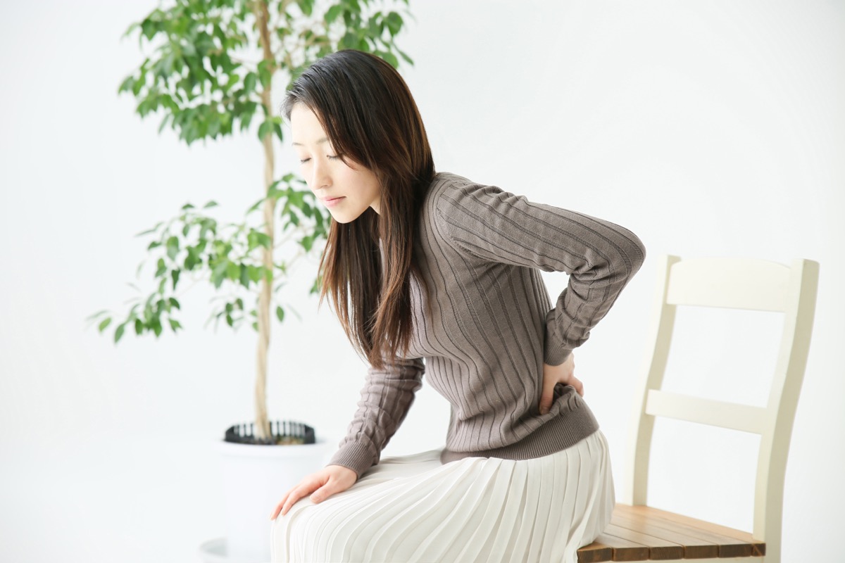 椅子から立ち上がるときに腰を押さえる女性