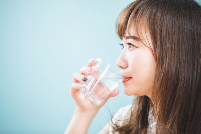 水色の背景の前で、透明なグラスの水を飲む女性の横顔
