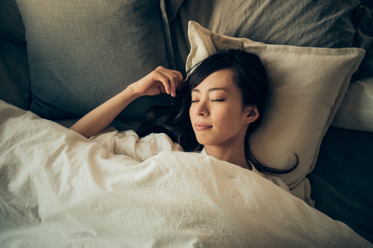 ベッドで白い掛け布団をかけ、目を閉じて眠る女性