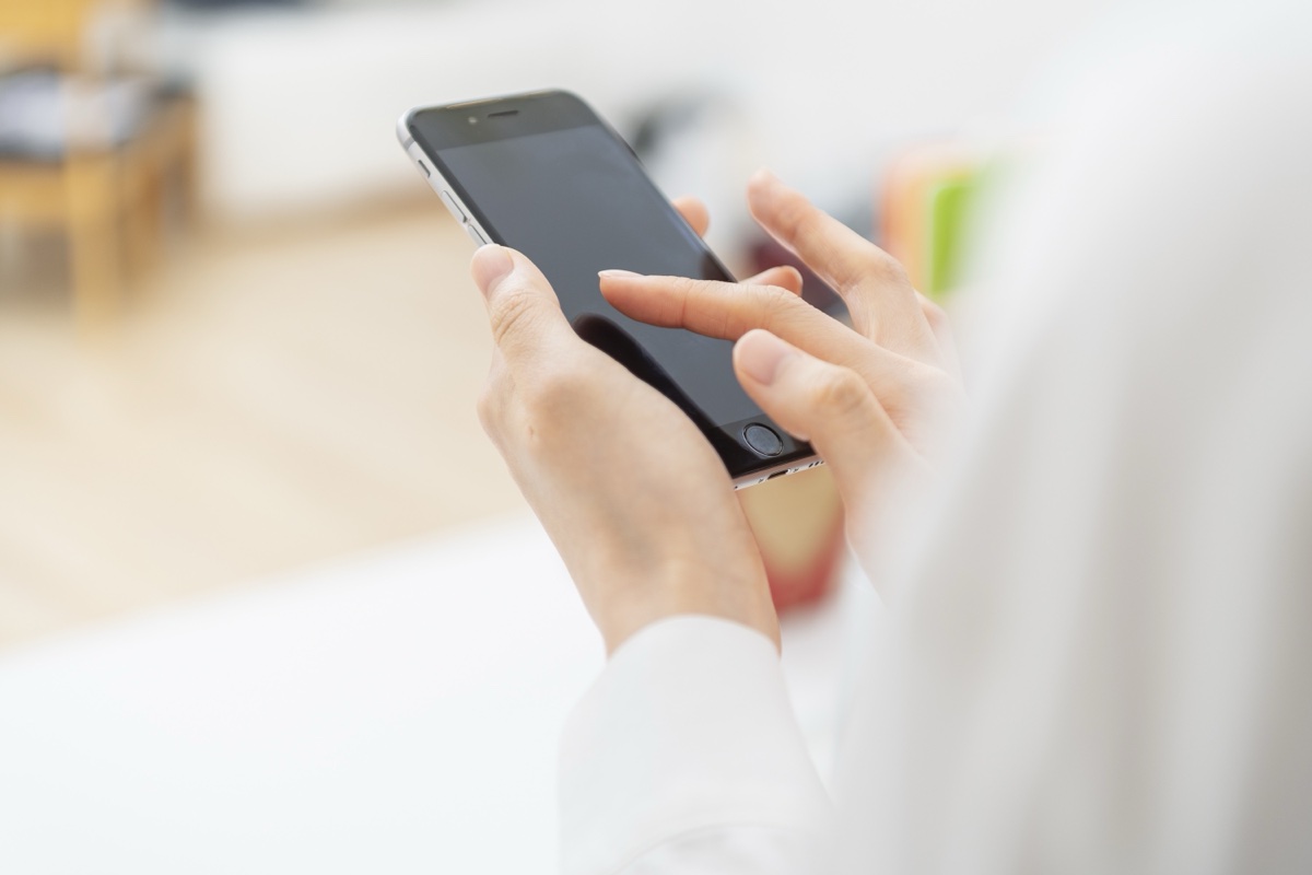 白い服の人がスマートフォンの画面を指で操作する手元