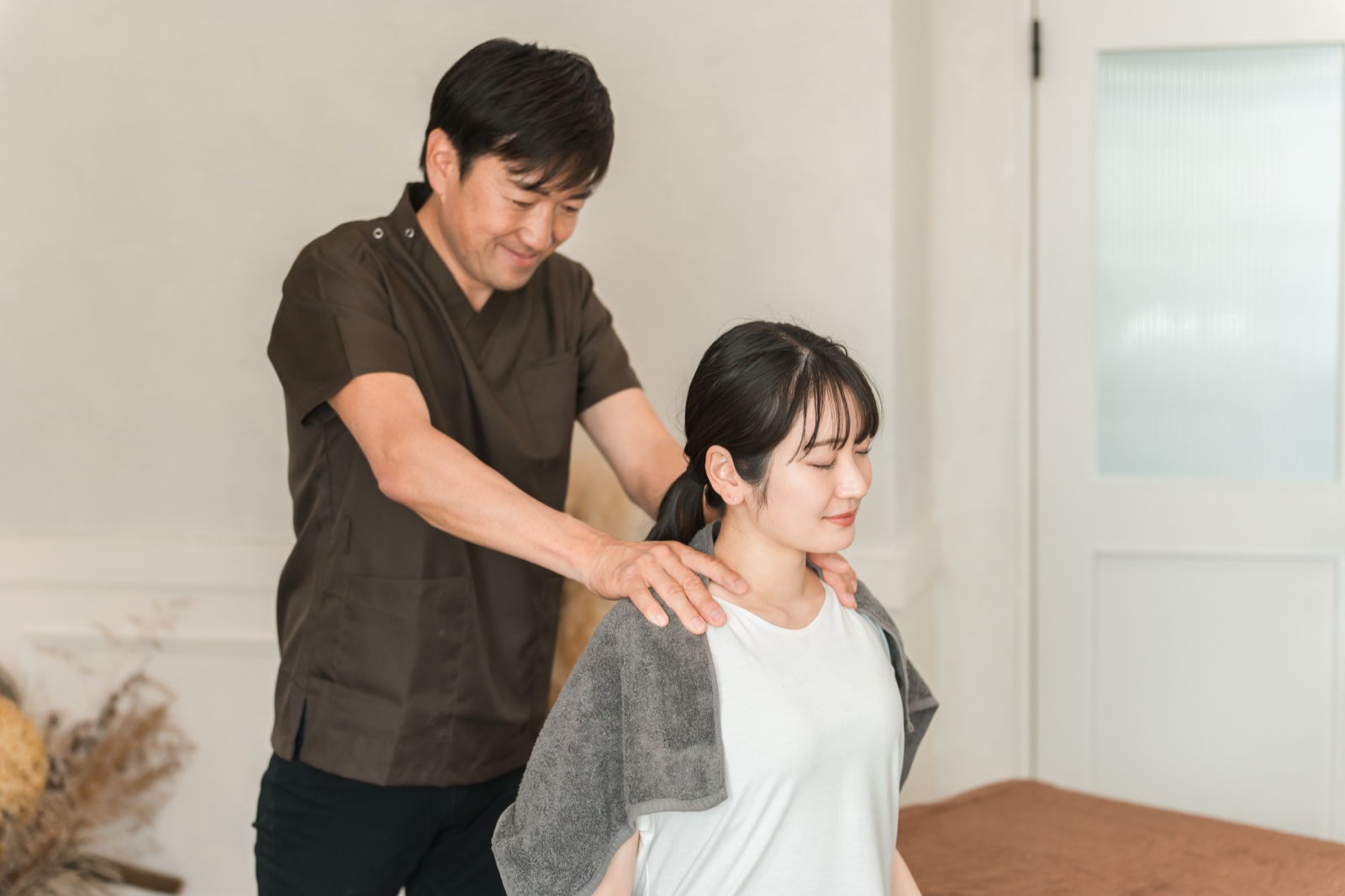 茶色の施術着の男性が座った女性の両肩に手を当てる