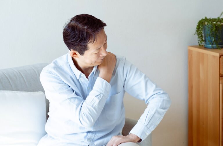 ソファに座り顔をしかめて左肩をつかむ男性