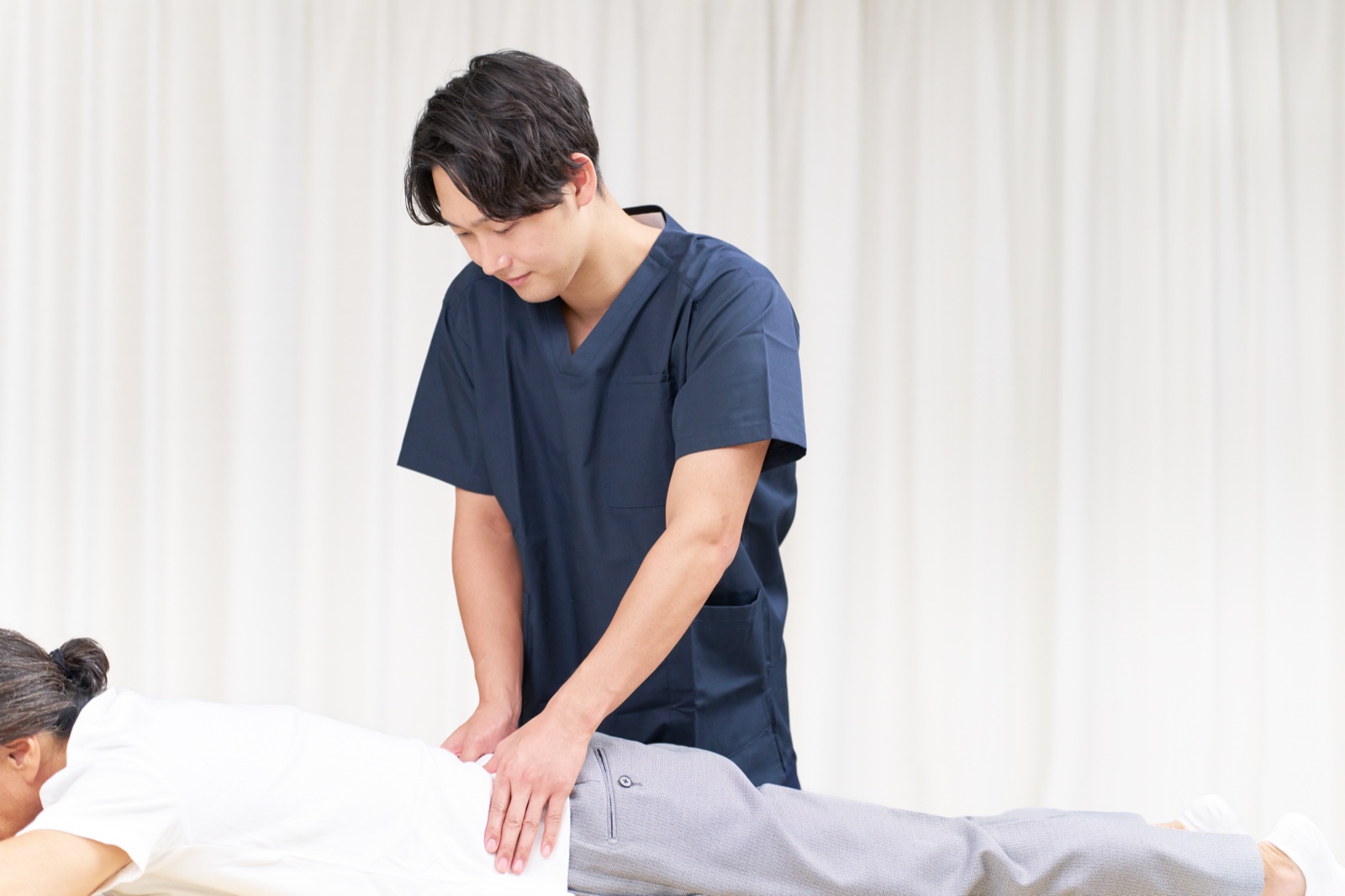 紺の施術着の男性がうつぶせの女性の腰に両手を当てる