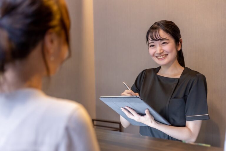 黒い半袖の制服の女性がタブレットを手に笑顔で話す