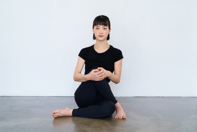 床に座り、立てた片膝を両手で抱える黒い服の女性