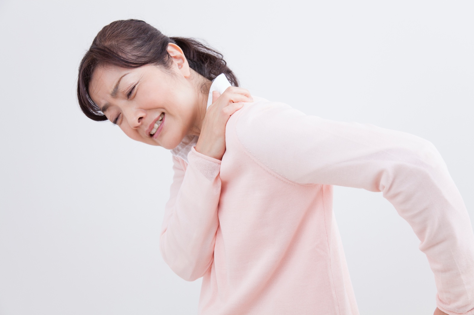 ピンクのセーターの女性が顔をしかめて左肩を押さえる
