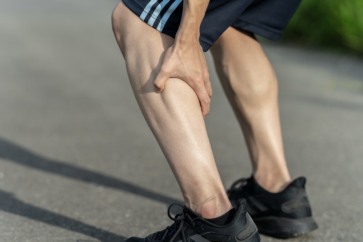 屋外で前かがみになり、ふくらはぎを片手でつかむ男性
