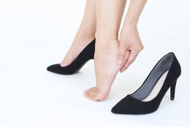 黒いパンプスを片方脱ぎ、かかとに手を当てる女性の足元