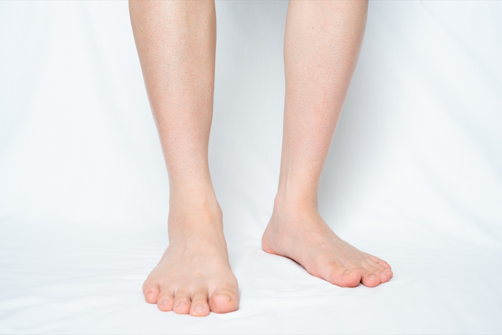 白い布の上に素足で立つ、すねから下の両脚
